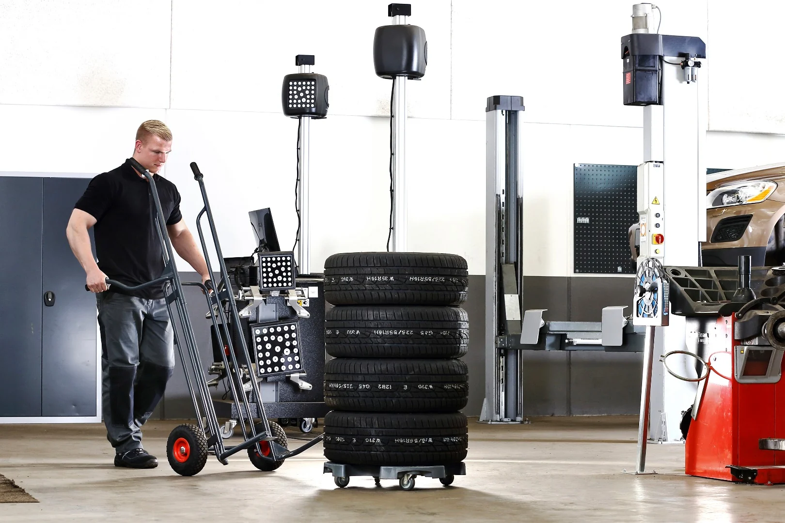 Mitarbeiter rollt den Wheel Caddy in einer Werkstatt an einen Reifenstapel auf einem Wheel Trolley heran