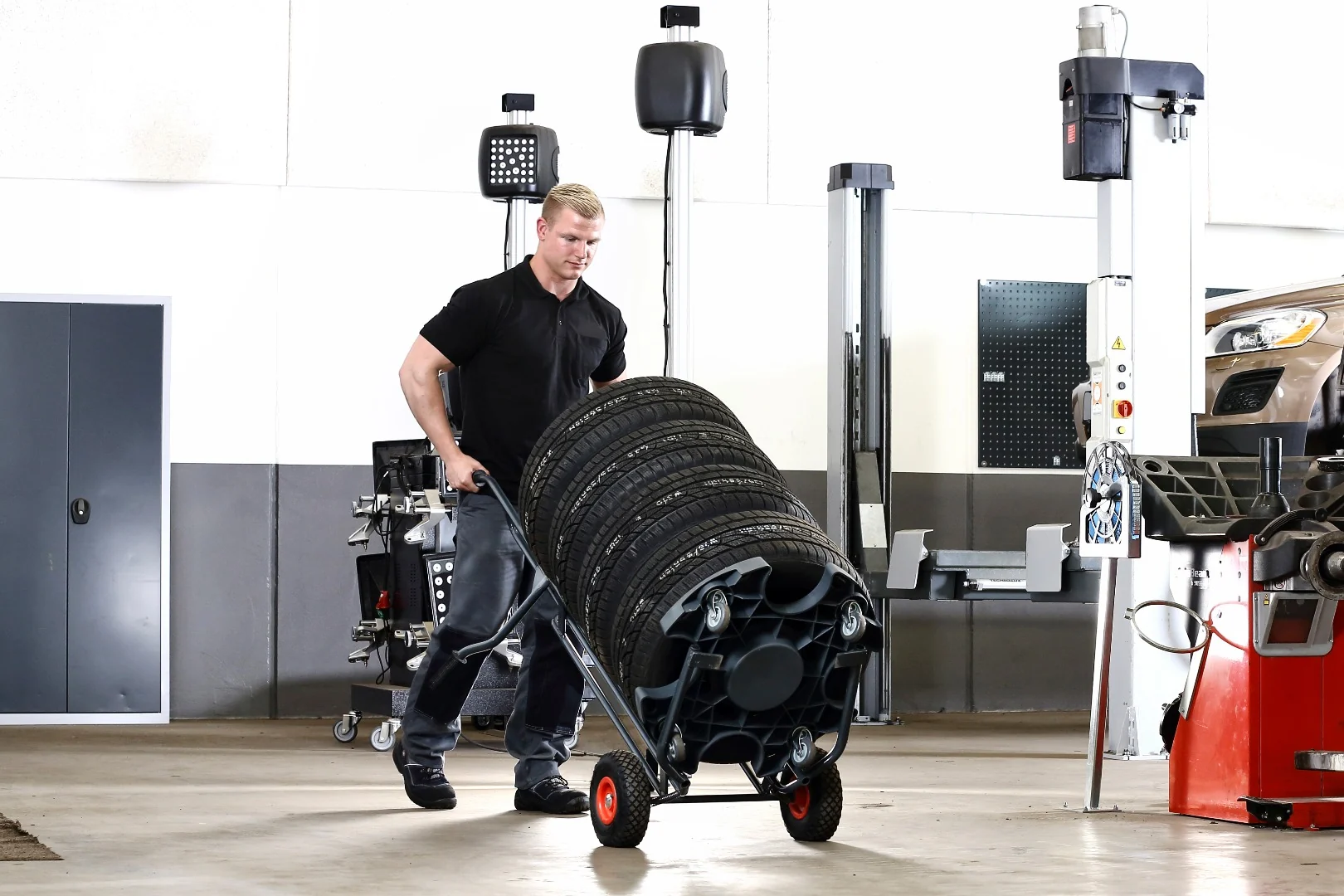 Mitarbeiter bewegt einen stark geneigten Reifenstapel auf dem Wheel Caddy durch die Werkstatt